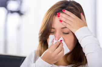 Woman holding tissue to nose.
