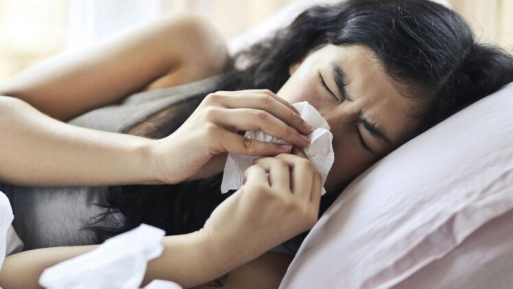 Woman lying in bet blowing her nose.