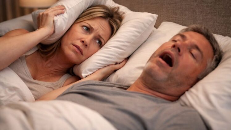 Man snoring loudly, while wife muffles sound with pillow.
