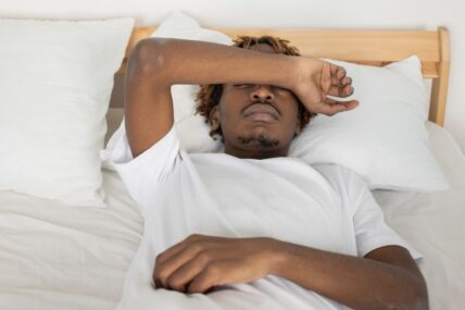 A man lying down and covering their eyes in bed.